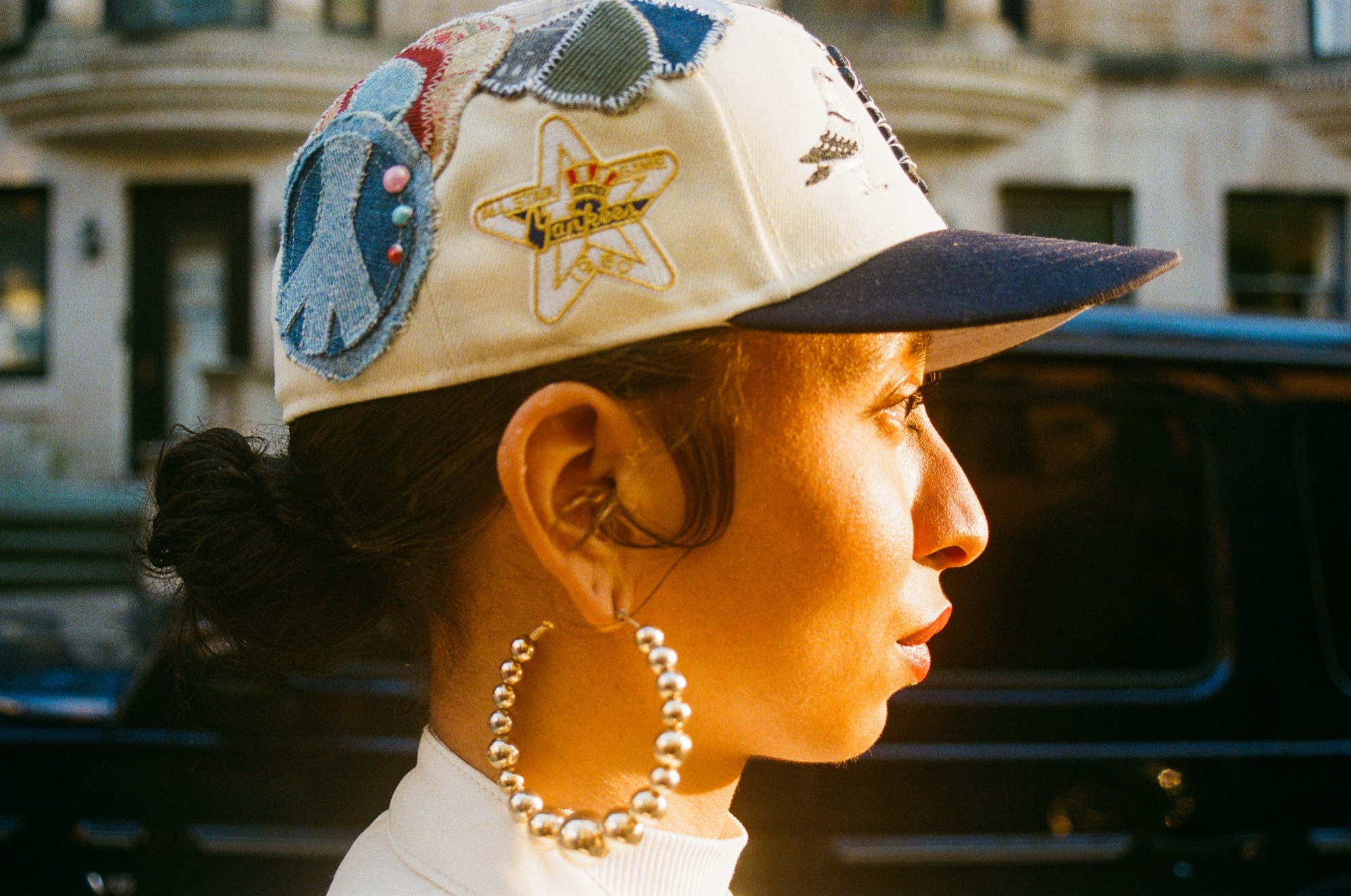 Profile portrait — patchwork cap and hoop earring at golden hour